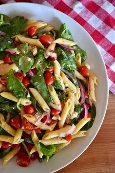 a white bowl filled with pasta salad on top of a wooden table next to a red and white checkered cloth