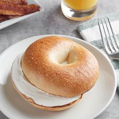 a bagel with cream cheese and bacon is on a plate next to a glass of orange juice