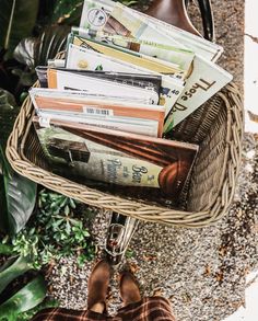 a person holding a wicker basket filled with books and magazines in front of some plants