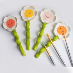 four painted flower shaped spoons with chopsticks in front of them on a white surface