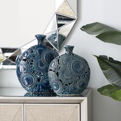 two blue vases sitting on top of a dresser next to a mirror and potted plant