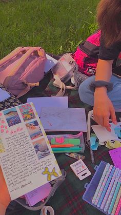 a person sitting on the ground with some art supplies in front of her and writing