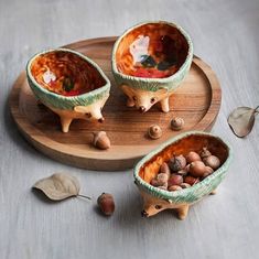 three ceramic bowls with food inside on a wooden tray next to leaves and acorns