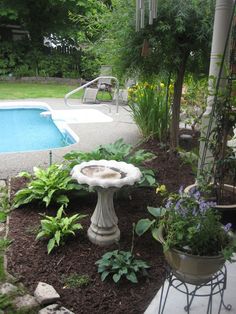 a small garden with a fountain in the middle and flowers around it near a swimming pool