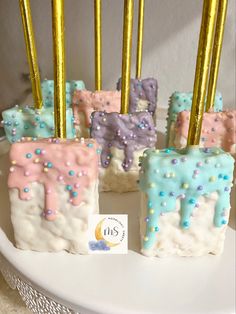 there are some cake like treats with gold sticks sticking out of the top and one is pink, blue, and white