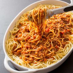 spaghetti being cooked in a white bowl with a ladle full of sauce and cheese