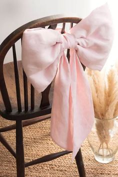 a pink bow sitting on top of a wooden chair next to a vase filled with feathers