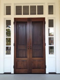 two wooden doors sitting next to each other in front of a white building with windows