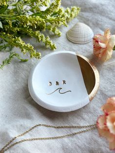 a white dish with the word d r written on it next to flowers and seashells