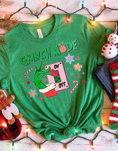 GRINCH MODE SHIRT - "Grinch Mode On Switch" Tee Get into the Grinch spirit with our "Grinch Mode On Switch" shirt! Perfect for spreading holiday cheer with a humorous twist, this tee is a fun addition to any Christmas wardrobe. Ideal for family gatherings or as a playful gift for the Grinch fan in your life. Product Features: Material: Crafted from 100% cotton for a soft, breathable feel. Sport Grey is a blend of 90% cotton and 10% polyester, Ash Grey has 99% cotton and 1% polyester, and Heather colors are a 50/50 blend of cotton and polyester. Fabric Weight: 5.0-5.3 oz/yd² (170-180 g/m offering a substantial yet comfortable feel. Fit: The unisex classic fit provides a structured look that pairs well with layered streetwear or casual outfits. Construction: Includes open-end yarn, tubular f Green Short Sleeve Shirt For Gift, Green Christmas T-shirt For Holiday, Green T-shirt For Christmas Holiday, Green Crew Neck Christmas Shirt, Green Christmas Letter Print Top, Green Holiday Top For Christmas, Green Long Sleeve T-shirt For Holiday, Green Holiday Tops With Letter Print, Holiday Green Tops With Letter Print