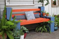 an orange and blue bench sitting in front of a house next to potted plants