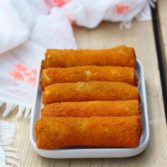 four deep fried food items in a white dish on a wooden table with cloths