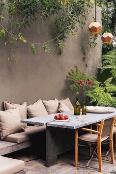 an outdoor seating area with tables and chairs in front of a concrete wall, surrounded by greenery