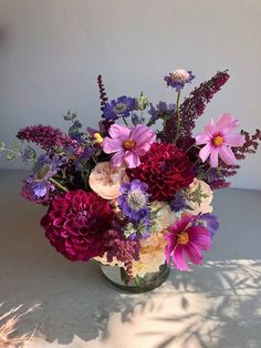 a vase filled with lots of purple and pink flowers on top of a white table