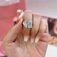 a woman's hand holding an engagement ring with two diamonds on it and a pink box in the background