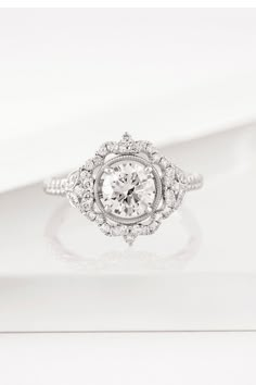 an engagement ring with a diamond center surrounded by small round brilliant cut diamonds on a white background