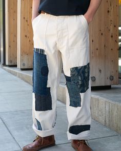 a man standing on the sidewalk with his hands in his pockets, wearing white pants and brown shoes