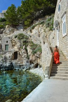 a woman in an orange dress is walking up some stairs to a building by the water