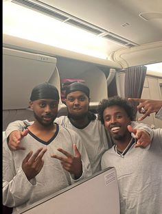 three men standing next to each other in front of a laptop computer on an airplane