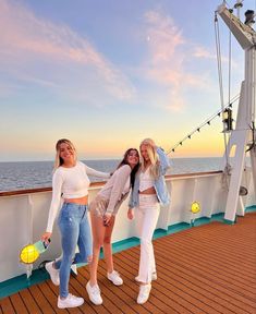 three women standing on the deck of a cruise ship at sunset, posing with their arms around each other