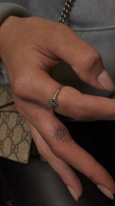 a woman's hand with a small tattoo on the middle finger and an eye ring