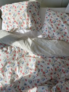 an unmade bed with white sheets and colorful flowers