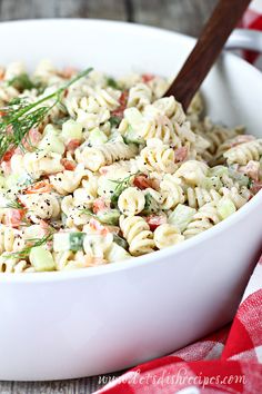 a white bowl filled with pasta salad on top of a red and white checkered table cloth