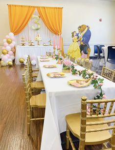 a table set up for a beauty and the beast themed birthday party with gold chairs