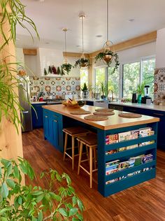 a large kitchen with blue cabinets and wooden flooring, surrounded by greenery on the walls