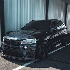 a black bmw suv parked in front of a metal building next to a parking meter