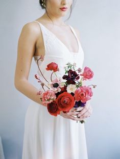 a woman in a white dress holding a bouquet of red, pink and purple flowers