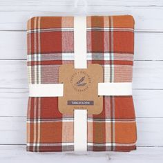 an orange and white plaid blanket sitting on top of a wooden floor next to a tag