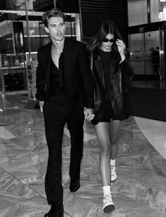 a man and woman walking down a hall holding hands, both wearing black jackets and white socks