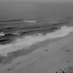 black and white photograph of the ocean with waves coming in from the shore, looking down on an empty beach