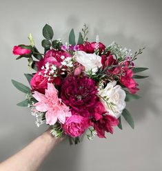 a hand holding a bouquet of flowers on a gray background with white and pink blooms