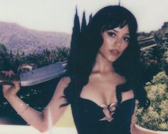 a woman in a corset holding a knife and posing for a photo with mountains in the background