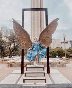 a woman in a blue dress is sitting on steps with wings spread over her body