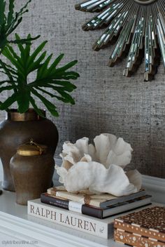 a white shelf topped with books and a vase filled with flowers next to a mirror