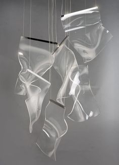 some clear plastic objects hanging from strings on a gray wall with light coming through them