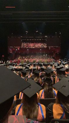 a large group of people in graduation gowns and caps at a stage with an audience