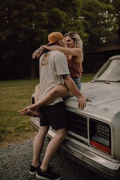 a man and woman leaning on the hood of a pickup truck while they are kissing