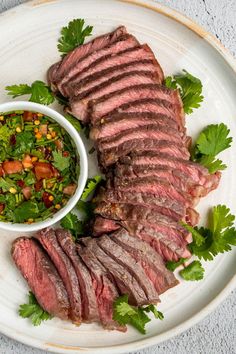 a white plate topped with meat and salad next to a bowl of dressing on top of it