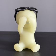 a white plastic toy with black glasses on it's head and nose, sitting in front of a gray background