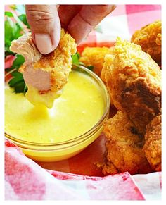 a person dipping something into a small bowl filled with sauce and chicken nuggies