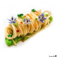 a pasta dish with broccoli and blue flowers on it's side is shown