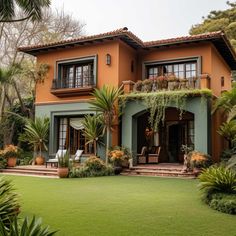 an orange and green house with lots of plants on the front lawn, surrounded by palm trees