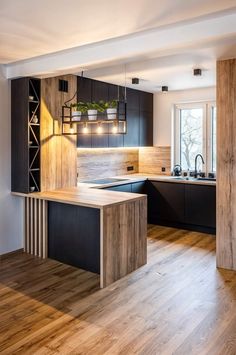 an open kitchen with wooden floors and black cabinetry is pictured in this image, there are lights hanging from the ceiling