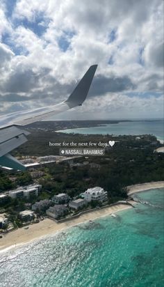 an airplane wing flying over the ocean next to a beach and houses in the distance