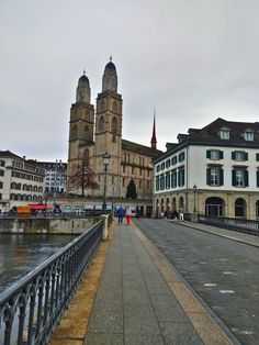 people are walking on the sidewalk near some buildings and a body of water in front of them