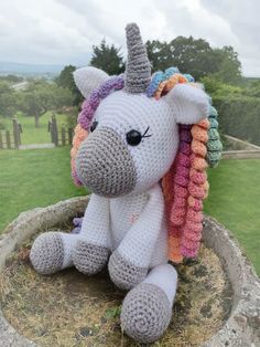 a crocheted stuffed unicorn sitting on top of a cement bowl